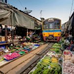 Treno giallo e blu della State Railway of Thailand che attraversa le bancarelle del mercato sulle rotaie di Maeklong