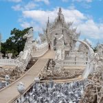 Veduta del ponte che attraversa il mare di mani scolpite verso l ingresso principale dell Ubosot bianco al Wat Rong Khun a Chiang Rai Thailandia